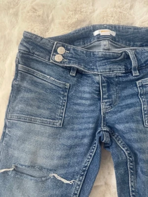 Blå slitna bootcut jeans - Säljer ett par ljusblå bootcut jeans från Gina 14+. De är i storlek S men uppsprättade längst ner så de är ca 3cm extra långa.💓