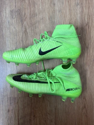 Nike Mercurial superfly - Säljer fotbollsskor från Nike, Mercurial Superfly-modell i neongrön färg. Ankelhög design med strumpliknande passform och snörning. 	•	Storlek: 42 	•	Underlag: AG (Artificial Grass)
