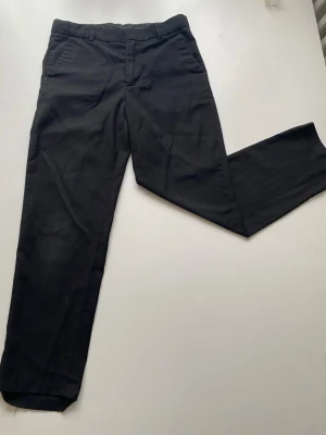 Svarta kostymbyxor med raka ben - Snygga svarta kostymbyxor med klassisk rak passform och pressveck. Byxorna har hällor för skärp, sidofickor fram och två passpoalfickor bak. Perfekta för en stilren look och passar till skjorta eller t-shirt.