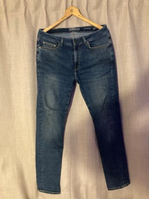 Mörkblå slim fit jeans Dressmann - Snygga mörkblå slim fit jeans från Dressmann med klassisk femficksdesign och dragkedjegylf. Jeansen har en smal passform och är perfekta för en stilren look. Materialet är denim med lätt stretch för extra komfort.