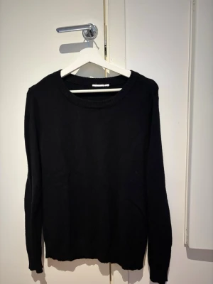 Svart basic stickad tröja - Enkel svart stickad tröja med rund halsringning och långa ärmar. Perfekt att matcha med jeans eller kjol för en clean look. Tröjan har ribbade muddar vid ärmslut och nederkant. 