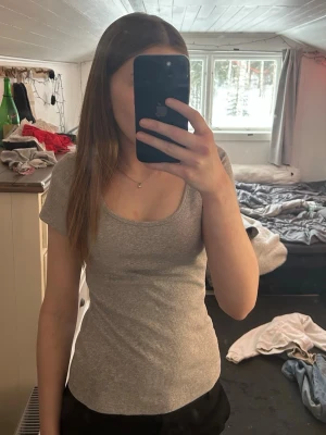 Grå ribbad t-shirt med rund hals - Säljer en enkel och stilren grå ribbad t-shirt med kort ärm och rundad halsringning. T-shirten har en tight passform och är perfekt för en avslappnad look. Passar till det mesta och är superbekväm.