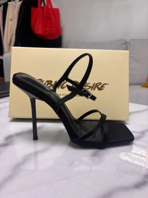Svarta stilettosandaler Public Desire - Snygga svarta stilettosandaler från Public Desire  med tunna remmar och dem har justerbart spänne vid ankeln. Dem är helt nya och oanvända, skickas även i original sko box, Pris går att diskutera. 
