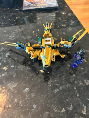 Lego Ninjago gyllene drake - Säljer en Lego Ninjago gyllene drake med gröna och svarta detaljer. Draken har rörliga vingar, huvud och ben samt plats för en minifigur. Två minifigurer ingår, en i grönt och guld och en i svart och lila. Perfekt för dig som gillar Ninjago och byggleksaker.