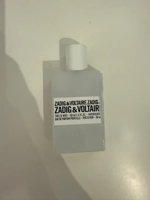 Zadig & Voltaire This Is Her! 50ml parfym - Minimalistisk och stilren parfymflaska från Zadig & Voltaire, modellen This Is Her! Flaskan är vit och rektangulär med svart text på etiketten. Parfymen är en Eau de Parfum för henne och rymmer 50 ml. Perfekt för dig som gillar moderna och unika dofter.
