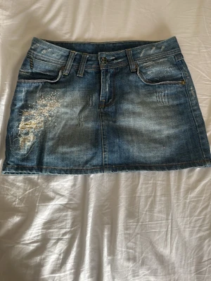 Blå jeanskjol med slitningar och nitar - Snygg blå jeanskjol i minilängd med slitna detaljer och små nitar på fram- och bakfickor. Kjolen har bälteshällor, klassiska fickor och en rak passform. 💗