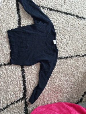 Mörkblå stickad tröja Newhouse - Mörkblå stickad tröja från Newhouse med v-ringad hals och ribbade muddar vid ärmslut och nederkant. Klassisk och enkel design som passar till det mesta. Perfekt för lager på lager och snygg till både jeans och kjol. Den är i storlek M men är liten i storleken så skulle säga att den passar mer xs-s! Har aldrig använt!