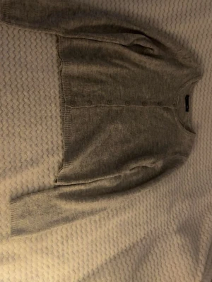 Ljusgrå kofta med knappar och storlek S - Mysig ljusgrå kofta med rund halsringning och knäppning framtill. Tillverkad i mjukt stickat material och har långa ärmar samt ribbade muddar vid ärmslut och nederkant. Perfekt att slänga över en topp för extra värme.