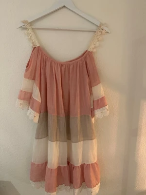 Randig sommarklänning med spetsdetaljer - En rosa, vit och beige randig strandklänning. Väldigt lätt och luftig. Storlek S/M. Liten gul missfärgning vid axelbanden. 