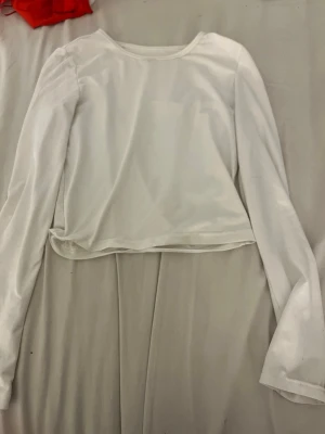 Vit croppad långärmad topp - En enkel och stilren vit croppad topp med långa ärmar och rund halsringning. Perfekt att matcha med jeans eller kjol för en clean look. Materialet känns mjukt och stretchigt, troligen bomull eller polyester.