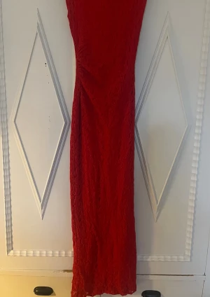 Röd lång spetsklänning - Snygg röd långklänning med spetsdetaljer och slits bak med en figurnära passform. 