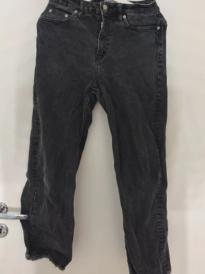 Svarta raka jeans med råa kanter - Säljer ett par svarta jeans med rak passform och råa, fransiga benslut. Jeansen har klassisk femficksdesign och hög midja. Perfekta för en avslappnad och trendig look. Materialet är denim i bomull.