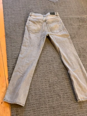 Ljusgrå raka jeans - Säljer ett par ljusgrå jeans med rak passform och klassiska fem fickor. Jeansen har bälteshällor och stängs med dragkedja och knapp. Perfekta för en avslappnad stil och lätta att matcha med olika outfits.