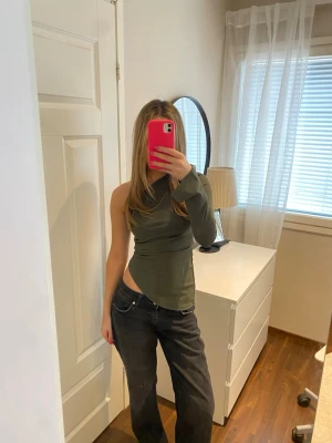 Mörkgrön oneshoulder topp - Snygg mörkgrön oneshoulder topp med lång ärm på ena sidan och axelbandslös på andra. Figurnära passform och trendig design som sticker ut. Perfekt att styla med jeans eller kjol för en cool look. Size XS