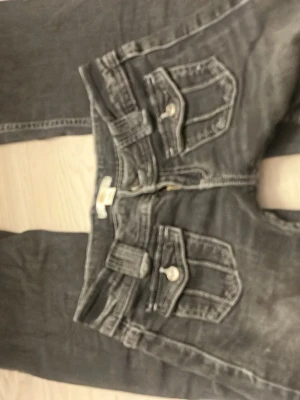 Grå jeans med fickdetaljer - Säljer ett par grå/svarta Gina tricot jeans med unika knappar där fram. Säljer pga för små storlek. Inte jätte använda och väldigt bra skick! Skulle passa till dig som vill ha en skön men fin Stockholmsstil. Kontakta gärna vid intresse!  Storlek 146.
