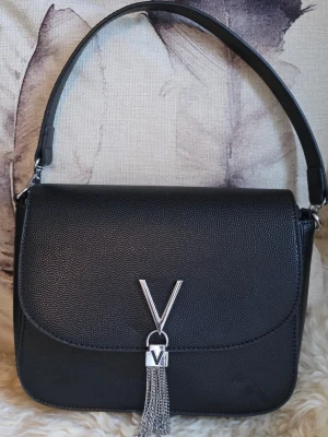 Valentino - Snygg svart handväska från Valentino med silverfärgad V-detalj och dekorativa kedjor framtill. Väskan har en stilren, fyrkantig form och är gjord i strukturerat konstläder. Perfekt accessoar för att lyfta din outfit. Väskan är i fint skick. 