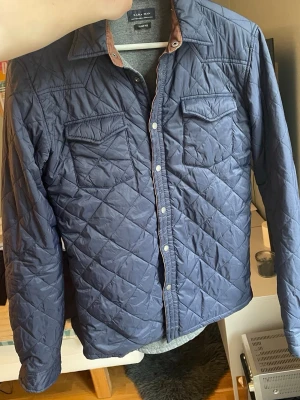 Blå Field jacka  - Snygg blå quiltad overshirt från Zara Man med tryckknappar och två bröstfickor med lock. Overshirten har en klassisk krage med kontrastfärg på insidan och är tillverkad i ett lätt vadderat material som ger en modern look storlek xs.