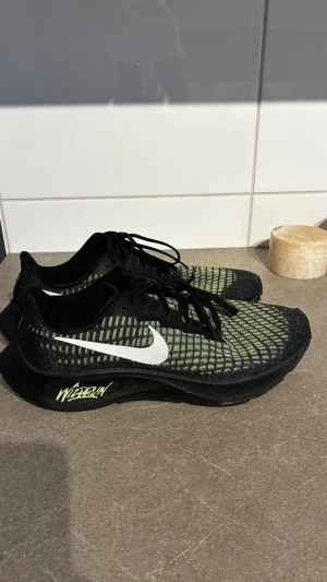 Nike Zoom svart/grön sneakers - Säljer ett par Nike Zoom sneakers med svart mesh och gröna detaljer. Skorna har en vit swoosh på sidan och texten 'WE RUN' på sulan. Låg modell med snörning och sportig design, perfekt för dig som gillar att sticka ut. Använd 2 gånger max! Som nya! Perfekta löpar skor elle ha dom dom inne skor på gymmet 🤩