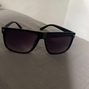 Svarta solglasögon med bred båge -  Rayban liknande Stilrena svarta solglasögon med bred, fyrkantig båge och mörka glas. Perfekta för att ge en cool touch till din outfit. Klassisk design som passar de flesta ansiktsformer.