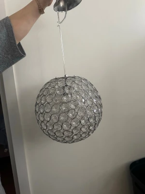 Glittrig rund taklampa i metall - Säljer en rund taklampa med stomme i silverfärgad metall och inslag av glittrande, klara plastkristaller. Lampan har ett nätmönster av cirklar och ger ett lyxigt intryck. Perfekt som blickfång i rummet.