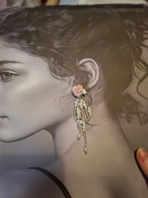 Örhängen med rosa ros och pärlor - Unika örhängen med en detaljrik rosa ros i plast och hängande kedjor av vita pärlor och små glaspärlor. Romantisk och lekfull design som sticker ut och ger en söt touch till din stil.