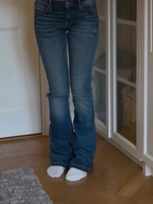 Blå bootcut jeans med slitningar från Crocker  - Säljer ett par blå bootcut jeans med lätt slitna detaljer och klassisk femficksdesign. Jeansen har en snygg tvätt och markerade sömmar. Perfekta för dig som gillar en avslappnad men trendig stil. Från Crocker 