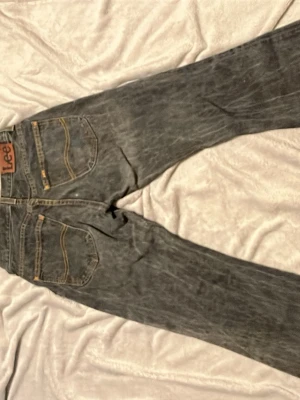 Svarta Lee jeans med raka ben - Säljer ett par svarta jeans från Lee med utsvängda ben och klassiska kontrastsömmar. Jeansen har fem fickor och Lee-lapp bak i midjan. Materialet är slitstarkt denim i bomull och passformen är relaxed fit. Perfekta för en avslappnad och cool stil.