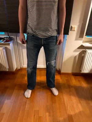 Levis 501 vintage Blå jeans - Säljer ett par blå jeans med rak passform och slitna detaljer på knäna. Jeansen har klassisk femficksdesign och är tillverkade i denim. Perfekta för en avslappnad och trendig look. Vintage 