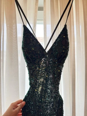 Mörkgrön festklänning med paljetter - Säljer nu min festklänning som endaste används en gång. Supersnygg mörkgrön långklänning med smala axelband och v-ringning. Klänningen är täckt av glittriga paljetter och har ett figurnära snitt som framhäver siluetten. Perfekt för dig som vill sticka ut på bal eller fest. Den är köpt för 4100 kr från L&S klänningaffär i Malmö. Och nu säljer jag den för 2000kr. Den är väldigt fin och detaljerad med paljetter, och även öppen i ryggen. 