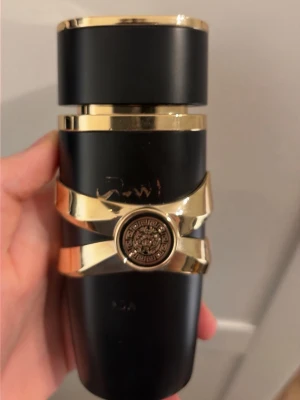 Svart och guld parfymflaska Lattafa - Elegant parfymflaska från Lattafa i svart och guld med en unik form och dekorativa detaljer. Flaskan har ett guldigt band runt mitten och ett emblem med arabisk text. Perfekt som lyxig accessoar på sminkbordet. Cirka 70ml kvar. Priset kan diskuteras.