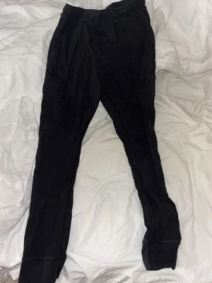 Svarta mjukisbyxor med dragsko - Ett par svarta mjukisbyxor med dragsko i midjan och muddar vid bensluten. Byxorna har en avslappnad passform och är tillverkade i ett mjukt, stretchigt material. Perfekta för chill dagar eller när du vill vara bekväm. 12-13Y