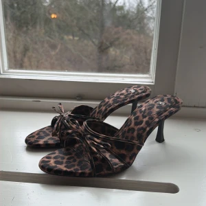 Leopardmönstrade pumps med smala remmar - Säljer ett par leopardmönstrade pumps från Zara med smala remmar och öppen tå. Skorna har en smal klack och trendig design som sticker ut. Perfekta för dig som vill ha ett statement-plagg i garderoben. Materialet är syntet och de har en snygg rosettdetalj framtill.