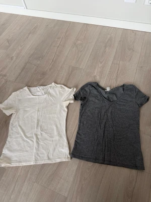 Två basic t-shirts i vitt och grått - Säljer två enkla t-shirts i basic stil, en i vit och en i grå färg. Båda har korta ärmar, perfekta till jeans eller shorts. Materialet känns mjukt och skönt. Den grå från hm och den vita från märket noa noa. 