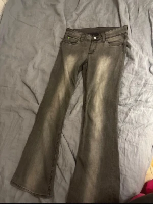 Cheap monday Grå bootcut jeans  - Säljer ett par grå bootcut och klassiska fem fickor. Jeansen har en låg midja och en liten grön detalj vid fickan. Perfekta för dig som gillar en avslappnad och trendig look. Jeansen är nästan aldrig använda.