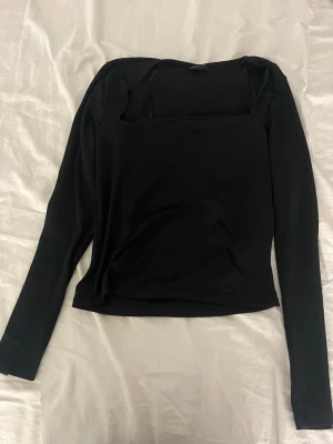 Svart långärmad topp Gina Tricot - Snygg svart långärmad topp från Gina Tricot med enkel och stilren design. Toppen har en rak passform och är tillverkad i ett mjukt material som känns skönt mot huden. Perfekt att matcha med jeans eller kjol för en clean look.