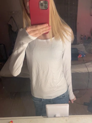 Vit långärmad topp i bomull - En basic vit långärmad topp i mjuk bomull. Enkel och stilren design med rund halsringning, perfekt att matcha med jeans eller kjol. Snygg passform som sitter bekvämt på kroppen.