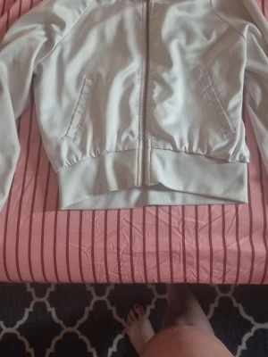 Ljusgrå bomberjacka med dragkedja - Snygg ljusgrå bomberjacka med dragkedja framtill och två snedställda fickor. Jackan har bred mudd i midjan och vid ärmsluten för en klassisk bomberlook. Perfekt för dig som vill ha en stilren och enkel jacka.