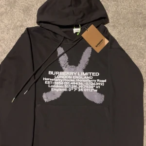 Svart hoodie från Burberry - Säljer en svart hoodie från Burberry med tryck i vitt och grått framtill. Stor logga och text på bröstet samt klassisk huva och magficka. Perfekt för sommaren/hösten tröja! Skick 10/10 helt oanvänd därför att den är för liten. Storleken är S. Om ni har några frågar så är de bara och höra av er MVH Melle. 