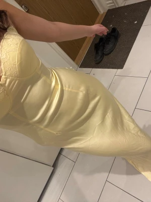 Ljusgul långklänning med spetsdetaljer - Supersnygg ljusgul långklänning med figurnära passform och spetsdetaljer upptill. Klänningen har bystparti med lätt struktur och smala axelband. Perfekt för dig som vill sticka ut med en elegant och feminin look. Använd en gång!