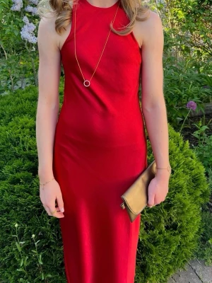 Röd långklänning - Säljer en elegant röd långklänning med hög hals och ärmlös design. Klänningen har en smickrande, figurnära passform och är tillverkad i ett glansigt material som ger en lyxig känsla. Perfekt för speciella tillfällen.