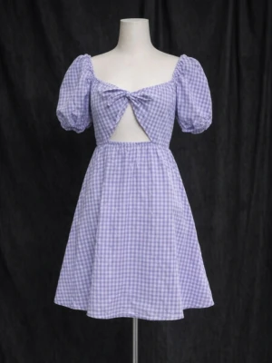 Lila rutig kortklänning med puffärm - Supersöt lila och vit rutig kortklänning med puffärmar, knyt framtill och en öppen detalj under bysten. Klänningen har en lätt utsvängd kjol och är perfekt för sommarens alla tillfällen. Trendig och ungdomlig look!