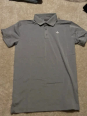 Grå pikétopp från Cross Sportswear - Klassisk grå pikétopp från Cross Sportswear med krage och knappar framtill. Tillverkad i mjuk bomullsmix och har korta ärmar för en clean och sportig vibe. Perfekt till jeans eller shorts för en enkel och stilren look.