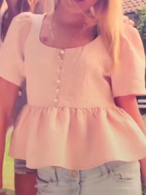 Rosa blus med pärlknappar - Supersöt ljusrosa blus med korta puffärmar och dekorativa pärlknappar framtill. Blusen har en volang nedtill och är tillverkad i ett strukturerat tyg som ger en lyxig känsla. Perfekt för dig som vill ha en feminin och trendig topp.Den passar mig som är 160/165cm