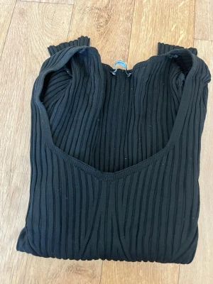 Svart ribbad långärmad topp - Snygg svart ribbad topp med lång ärm och v-ringad halsringning. Toppen har en figurnära passform och är tillverkad i ett stretchigt material som sitter skönt på kroppen. Perfekt att styla med jeans eller kjol för en trendig look.
