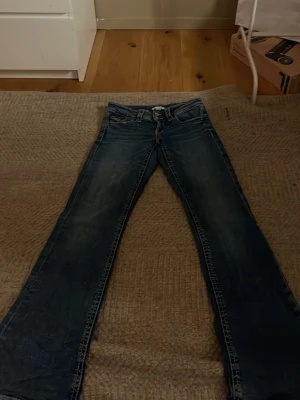 Blå bootcut jeans med vit söm - Säljer ett par blå bootcut jeans med klassisk femficksmodell. Jeansen har normalhög midja och är tillverkade i denim med snygg tvätt. Perfekta för dig som gillar en avslappnad men trendig look.