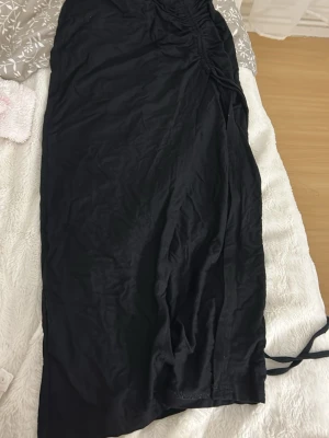 Svart och vit långkjol med snörning - Snygg svart och en långkjol med snörning i sidan som ger en cool rynkad effekt. Kjolen har en enkel och stilren design, perfekt att matcha med olika toppar. Materialet känns mjukt och följsamt mot kroppen.