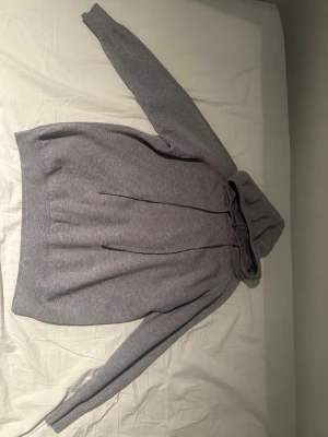 Grå hoodie med huva och dragsko - Mysig grå hoodie i mjukt stickat material med huva och dragsko. Långa ärmar och ribbade muddar vid ärmslut och nederkant. Perfekt för chill dagar och enkel att matcha med jeans eller mjukisbyxor.Den är för liten vill få bort, pris är diskuter bart.