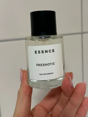 ESSNCE Freshotic Eau de Parfum -  parfymflaska från ESSNCE med doften Freshotic. Flaskan är genomskinlig med en enkel vit etikett och svart text, samt ett svart cylinderformat lock. Modern och stilren design som passar perfekt i badrumshyllan.