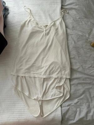 Pyjamasset - Säljer ett krämvitt ribbat pyjamasset från Ullared med smala axelband och knappdetalj framtill. Setet är tillverkat i ett mjukt och stretchigt material, perfekt för en avslappnad och bekväm stil. ECO-kollektion. Toppen är i 2xl och underdelen är i L!