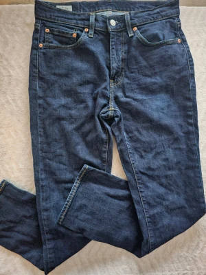 Levi's 514 mörkblå jeans - Säljer ett par klassiska Levi's 514 jeans i mörkblå denim med raka ben och fem fickor. Jeansen har kontrastsömmar, läderpatch bak och den ikoniska röda Levi's-taggen vid bakfickan. Perfekta för en avslappnad och stilren look.